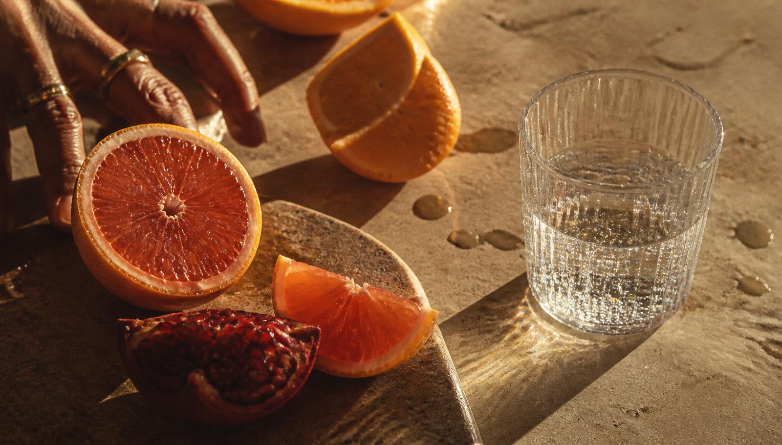 Sliced citrus and pomegranate on stone beside a glass of sparkling water in warm light